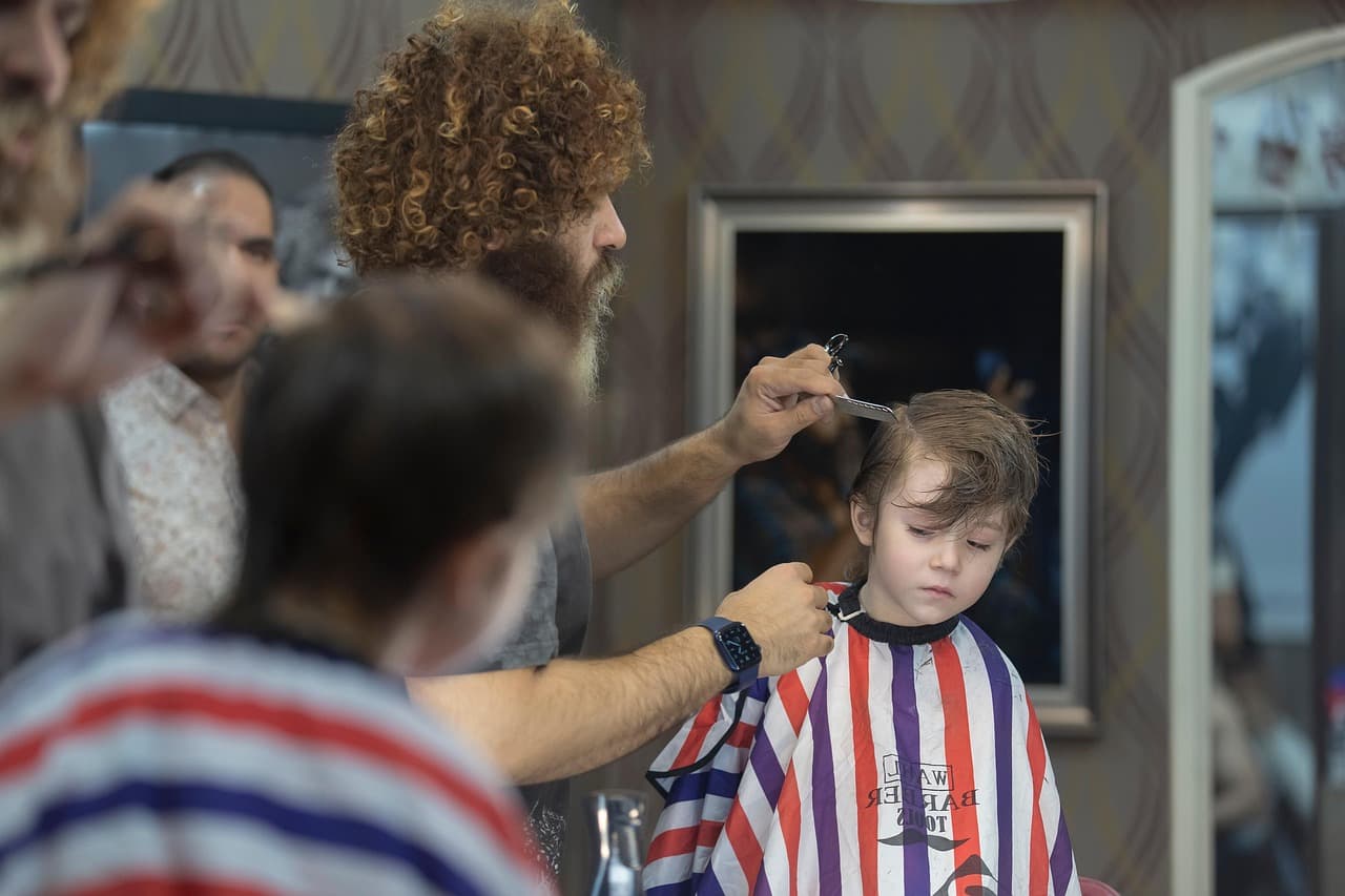 A barber cutting a young boy’s hair in a striped cape