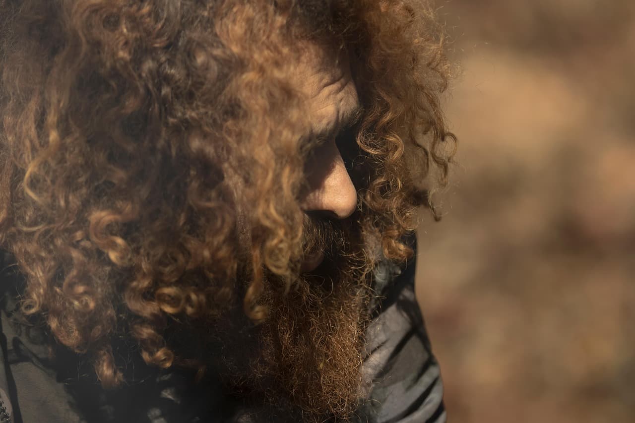 A man with long curly hair and a full beard, in profile